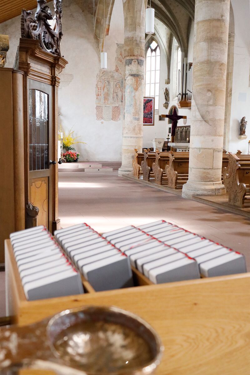 Blick in den Altarraum. Im Vordergrund Weihwasserbecken, Gotteslob-Bücher, Beichtstuhl